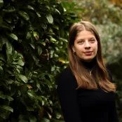 Head and shoulders portrait image of Paulina Borek, MA History student smiling and looking at the camera. She is outside, standing in front of dark green shrubs.