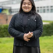 Xinyang Han is standing outside the University buildings, smiling at the camera.