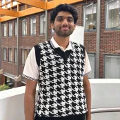Elvin Jinu, Aeronautical and Astronautical Engineering student standing on the balcony of one of the Universities’ modern buildings with brick and wood features.