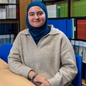 Nora Belkhiter, law student. is sitting at a desk in the law library, smiling at the camera.