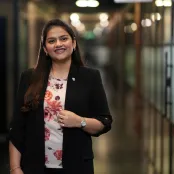 MA Luxury Brand Management graduate, Bhavna Sharma, is standing in a corridor smiling at the camera.