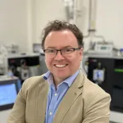 Professor Max Crispin smiling at the camera. He is standing in a lab with a lot of technical equipment in the background.