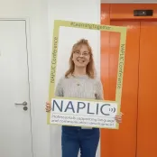 Modern languages and linguistics graduate, Bryony is holding and looking through an open frame. The frame advertises the NAPLIC conference - Professionals supporting language and communication development.