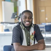 Applied GIS and Remote Sensing master’s student Bright, is sitting at a desk and smiling at the camera.