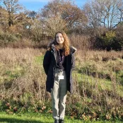 Applied GIS and Remote Sensing master’s student, Jessica, is standing in a field. The grass is long and trees in the background.