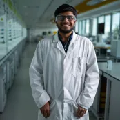 Advanced chemical engineering student Shantanu, wearing a white coat and safety glasses standing in a chemistry lab.