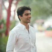 Law graduate and entrepreneur Rohit is standing looking to the right of the camera. There are out of focus trees and shrubs behind him.