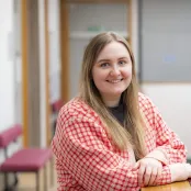 Psychology masters student Katie is leaning on a table and smiling at the camera.