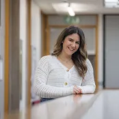 Psychology master’s student Zara is leaning on a table and smiling at the camera.