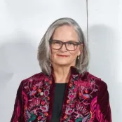 A portrait image of Professor Deborah Gill, Vice-President. She's wearing a patterned red jacket and smiling for the camera against a white background. 