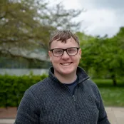 Smiling student wearing glasses standing outside the Physics building..
