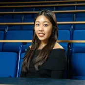 Student sitting in a lecture theatre, smiling at the camera.