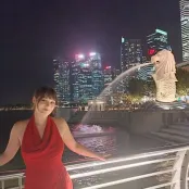 female student stood in front of railings with water feature and city skyline with lit up tower buildings against dark night sky in the background.