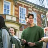 Two postgraduate students smiling at each other while walking outside the Parkes Building, also known as Building 65, on the University of Southampton's Avenue Campus. They are part of a larger group of students.