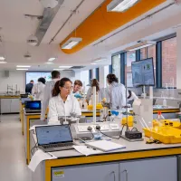Group of students working in a bright, modern, vibrant chemistry laboratory. Students tend to a variety of equipment and glassware on the benches.