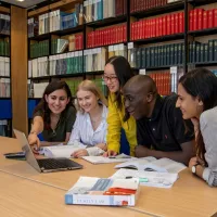 Students huddle around laptop in the library law collection