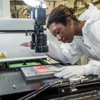 A student wearing protective clothing uses printed electronics and materials equipment