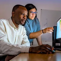 Two researchers stare intently at a screen with geographic information, one pointing to a specific area