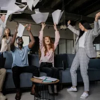A diverse group of business people throw sheets of paper in the air in a celebratory fashion