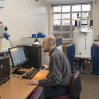 A man working  on a computer in a room with a Nuclear Magnetic Resonance machine in the background
