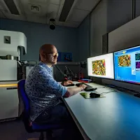 A scientist sits at a bank of computer screens performing scanning electron microscopy