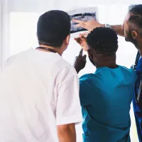 Three healthcare professionals examining an X-ray next to a window.