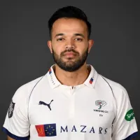 Azeem Rafiq in Yorkshire cricket shirt, facing camera against a dark background.