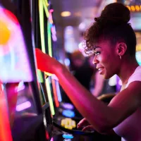 A woman playing a brightly lit slot machine in a casino.