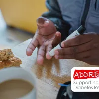 Person using a glucose meter on their fingertip beside a cup of coffee and biscotti on a table.