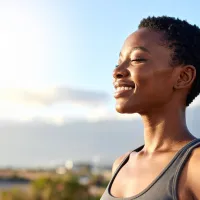 Person with short hair smiling with eyes closed against a bright sky background.