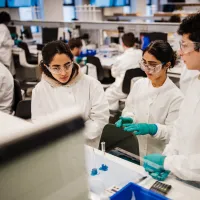 University students in lab coats and safety goggles working together in a modern science laboratory.