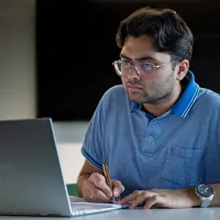 Business entrepreneurship student is reading his laptop and making notes in a notebook. 
