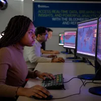 Finance and financial technology student seated at a desk using a keyboard and mouse, working on a computer displaying a world map with data points. 