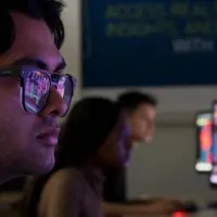A student in the foreground looks intently at his PC screen, business analytics reflected in his glasses