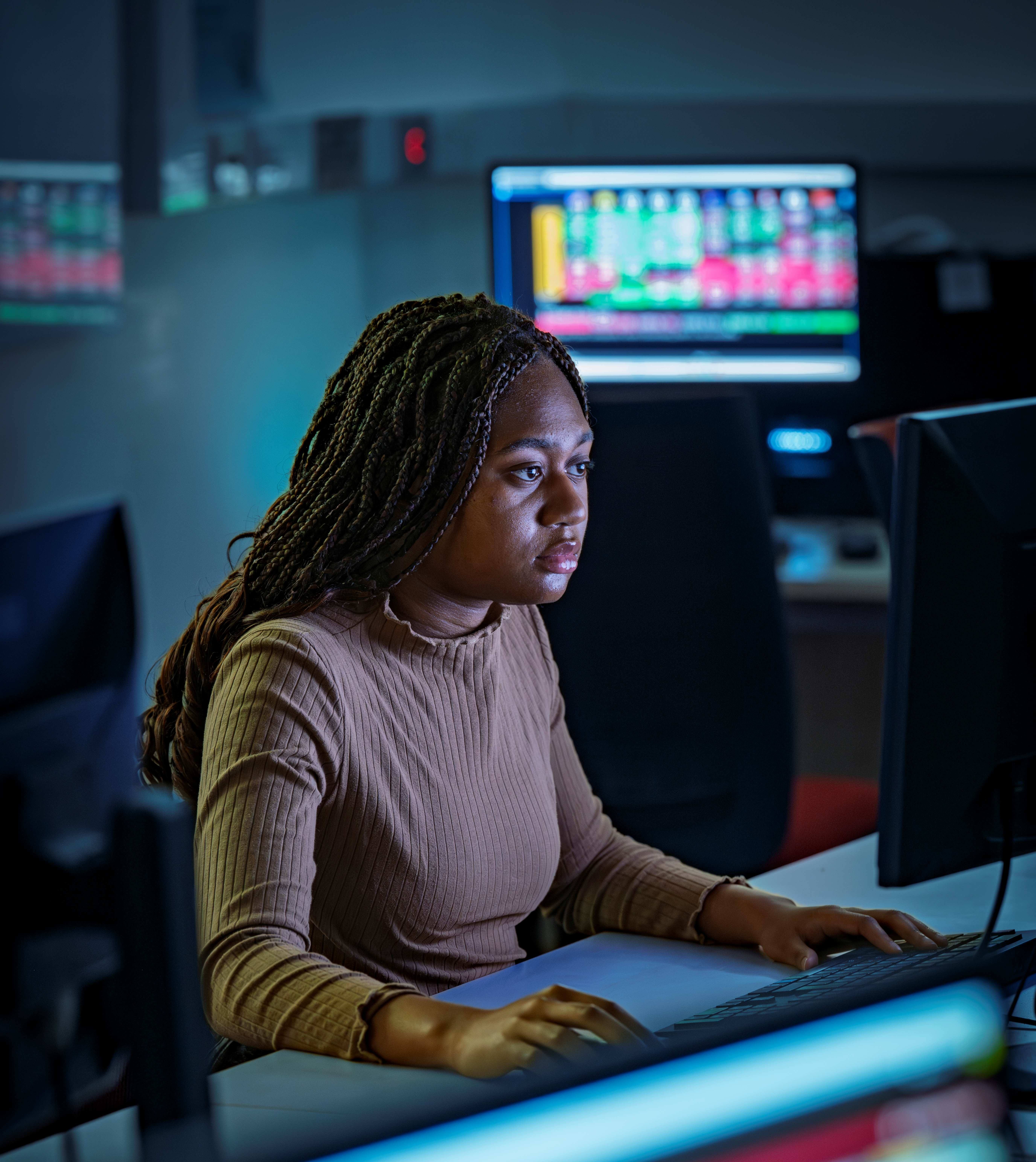 A student working in the financial lab. There are colourful screens showing data around the lab.
